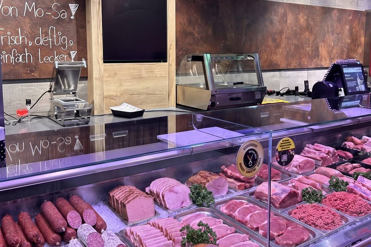 Die Fleischtheke: Wurst, Schinken, Steaks und Hackfleisch in der Auslage, darüber die Tafel „Frisch, deftig, einfach lecker!“.