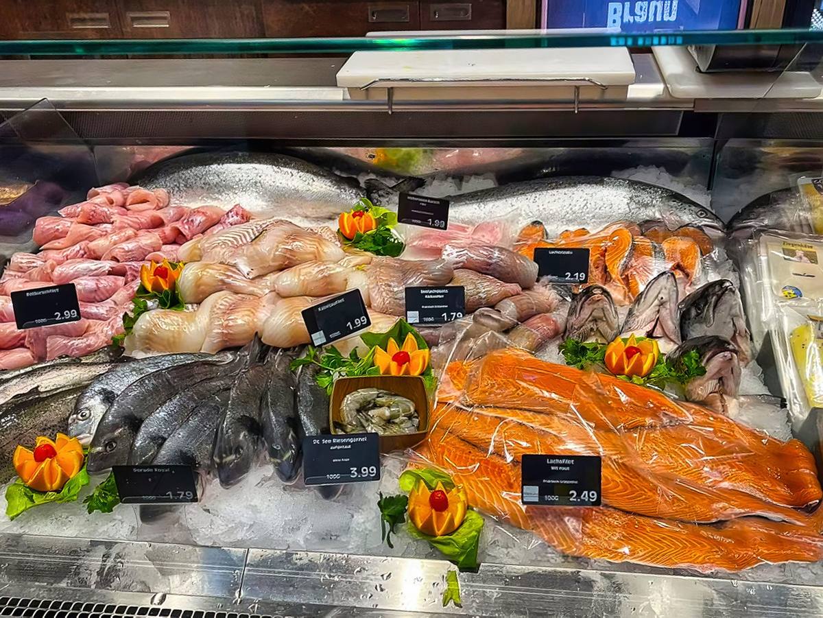 Die Fischtheke auf Eis: ganze Doraden und Forellen, Lachsseiten, Filets und Garnelen, dazwischen kunstvoll geschnittene Orangen als Garnitur.