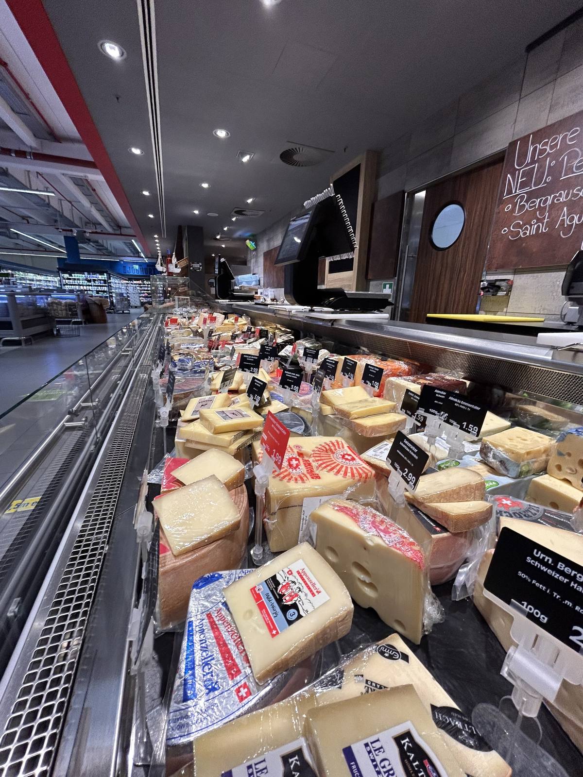 Nahaufnahme der Käseauslage: Hartkäsestücke, Weichkäse und Spezialitäten dicht an dicht in der gekühlten Vitrine.