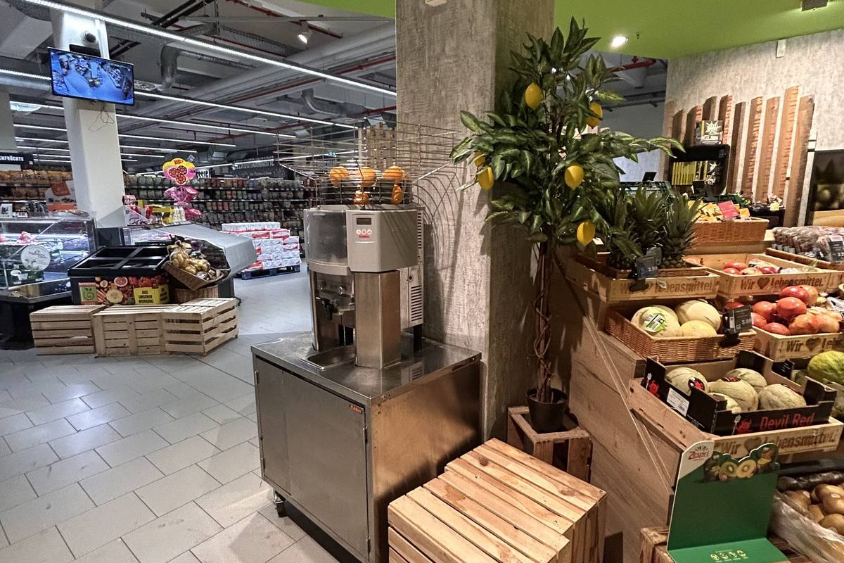 In der Obstabteilung steht ein Zitronenbäumchen neben der Saftpresse und gestapelten Holzkisten mit Melonen und Ananas.