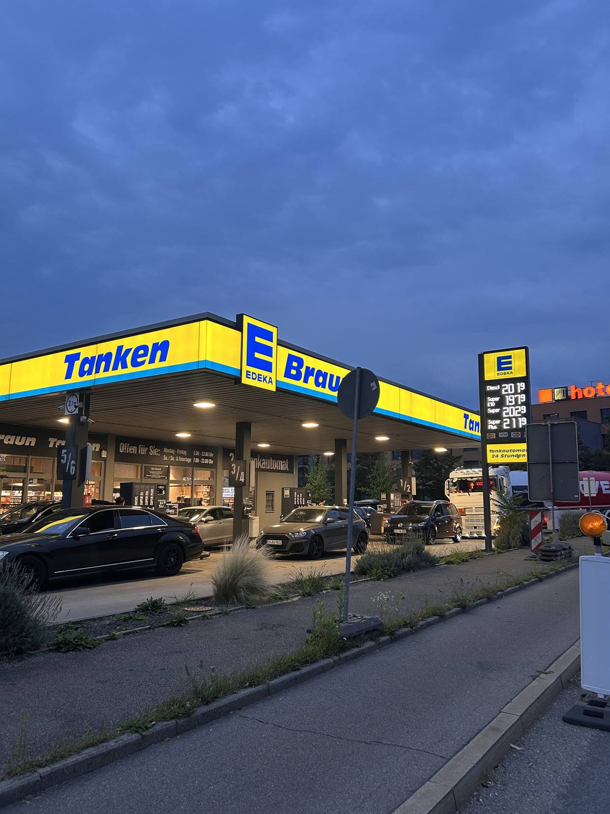 Die Tankstelle des Marktes in der Dämmerung: das beleuchtete gelbe Dach mit dem Schriftzug Tanken E Braun über den Zapfsäulen.
